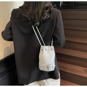 Sac seau en similicuir gris clair avec cordon et boucle, porté par un mannequin