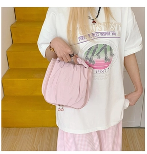 Pink fabric makeup bag with pearl zipper detail held against a yellow background