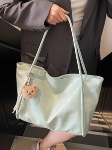 Light mint green soft leather tote bag with bear charm shown on model in stairwell