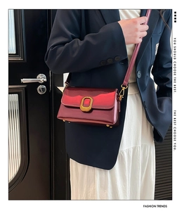 Détail d'un sac en cuir verni bordeaux avec boucle dorée porté sur une veste bleue