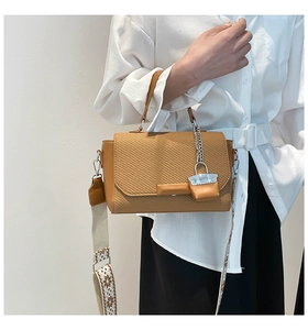 Detailed view of woven texture and chain ornament on a camel brown leather crossbody bag