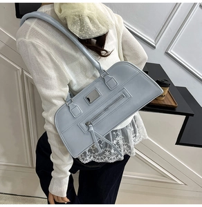 Détail du sac à épaule en cuir bleu clair avec poche zippée avant et plaque métal