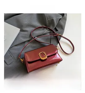 Détail d'un sac à main en cuir verni bordeaux avec boucle en métal doré sur veste grise