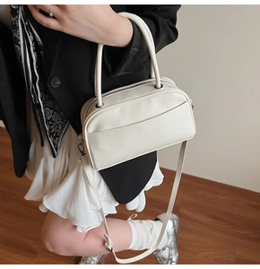 Detail view of a cream Boston bag featuring cylindrical handles and a side shoulder strap