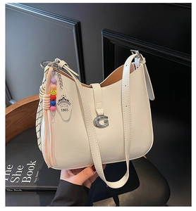Detail of white leather crescent bag with silver G-buckle and beaded charm accessory