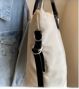 Détail d'un grand sac fourre-tout beige avec bandoulière noire et boucles métalliques argentées