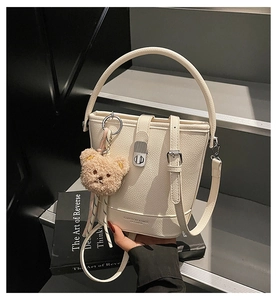 Detail of white lychee leather bucket bag with silver lock and plush bear charm
