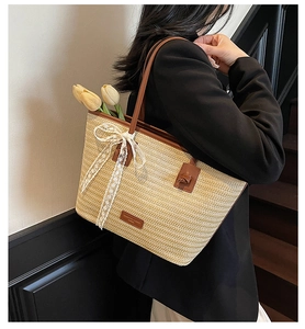 Détail d'un sac cabas en paille avec lanières en cuir marron et nœud en dentelle blanche