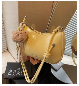 Detail of yellow patent leather crescent shoulder bag with cute brown plush bear charm