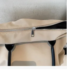 Détail de la fermeture éclair argentée et des poignées noires sur un sac fourre-tout beige