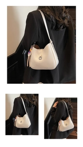 Detail of cream patent leather half-moon bag with gold G-buckle and colorful charm