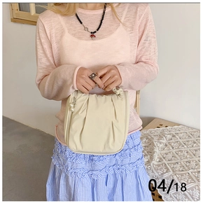 Detail of off-white pleated handbag with pearl charm and soft textured synthetic leather