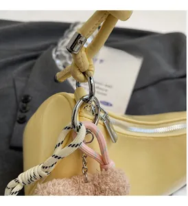 Detail of yellow glossy leather handbag with braided rope handle and plush charm