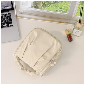 Detail of cream makeup bag with pleated handle and pearl zipper pull on a desk