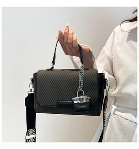 Detail of black woven flap handbag with geometric patterned wide shoulder strap and charm