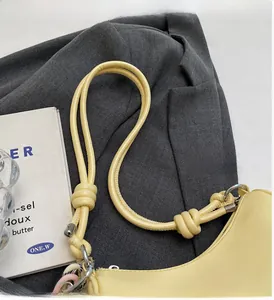 Detail of creamy yellow shoulder bag showing cylindrical strap with knot and silver hardware