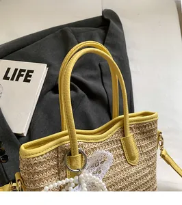 Detail of hand-woven straw bucket bag with yellow leather trim and pearl bow charm
