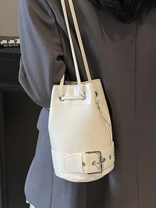 Sac seau chic en cuir ciré blanc crème porté sur un costume gris pour un look moderne