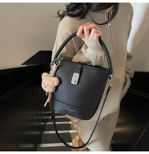 Detail of black lychee grain leather bucket bag with silver twist lock and bear charm
