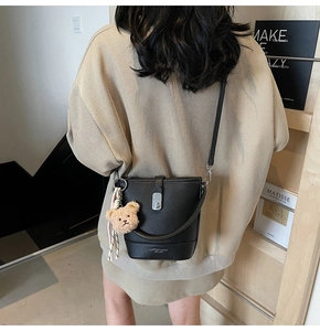 Detail of black lychee grain leather bucket bag with bear charm and silk scarf decoration