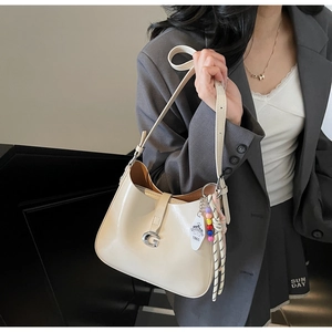 Detail of cream patent leather underarm bag featuring a silver G-buckle and beaded charm