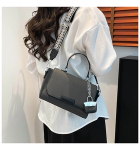 Detail of elegant black leather handbag with woven flap and jacquard wide shoulder strap