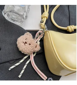 Pink plush bear head charm accessory with woven strap on a stylish yellow handbag