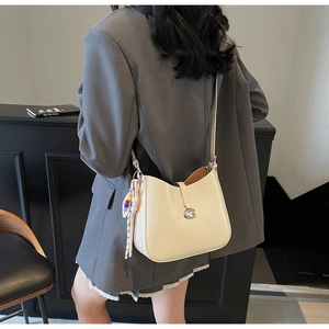 Detail view of cream patent leather bag with silver G buckle on a model in a gray suit