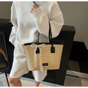Détail d'un sac cabas en paille avec poignées en cuir noir et décoration de nœud en dentelle