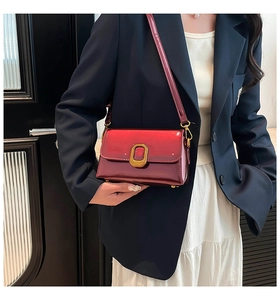 Détail du sac bandoulière en cuir verni rouge foncé avec boucle dorée sur une tenue bleue