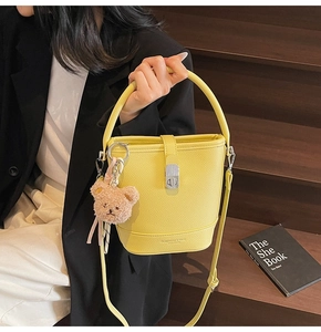 Detailed side view of yellow bucket bag with teddy charm and silver metal twist lock