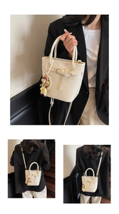 Detail of cream bucket bag with litchi texture, bow buckle, and cute doll pendant accessory