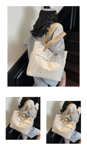 Detail of off-white canvas tote bag with yellow embroidery and khaki straps on a model