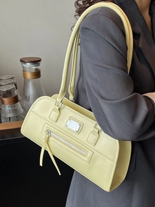 Sac sous l'aisselle minimaliste en cuir jaune pâle avec plaque en métal sur modèle gris