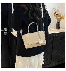 Detail view of beige woven handbag with chain pendant and wide strap shown on model