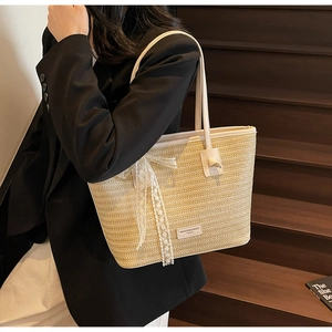 Détail du sac cabas en paille beige avec nœud en dentelle blanche et anses élégantes