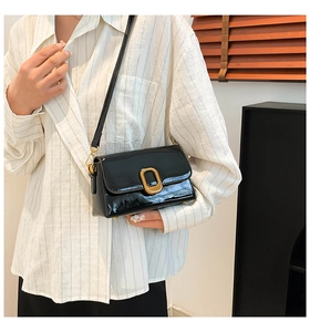 Détail d'un sac bandoulière chic en cuir verni noir avec boucle dorée sur un mannequin