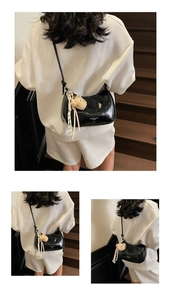 Detail of black patent leather crescent bag with plush bear charm and knotted shoulder strap