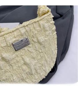 Detail of beige pleated fabric texture with silver rectangular metal logo plate on a bag