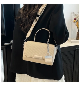 Detail of beige woven texture handbag with jacquard strap and mini charm accessory