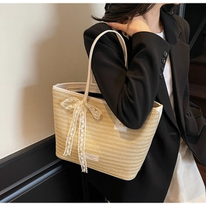 Détail du sac cabas en paille beige avec nœud en dentelle blanche et finitions cuir