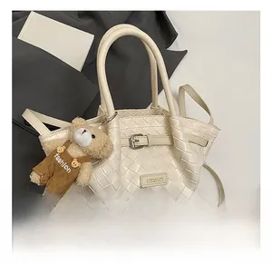 Close-up of cream woven handbag with metal buckle, brand logo, and a cute teddy bear charm