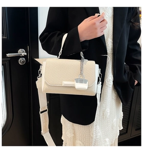 Detail of cream woven handbag with wide shoulder strap and mini metal chain charm accessory