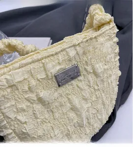 Detail shot of the pale yellow pleated texture and silver metal brand plate on the chic bag