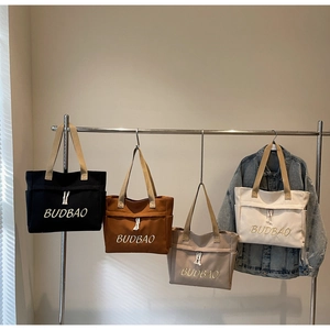 Detail of four colorful canvas tote bags with side pockets and BUDBAO logo hanging on a rack