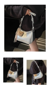 Detail view of silver crescent shoulder bag featuring knotted strap and plush bear charm