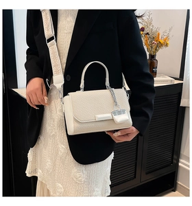 Close-up of cream textured flap bag with woven pattern and wide jacquard strap