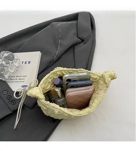 Spacious interior of yellow ruched cloud bag holding phones, wallet and perfume bottles