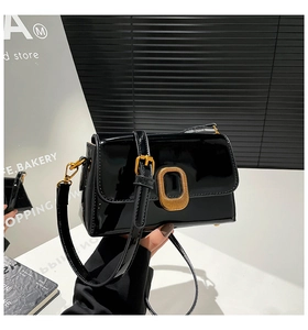 Gros plan d'un sac bandoulière en cuir verni noir avec une boucle dorée rectangulaire