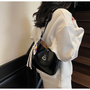Detail of black patent leather underarm bag featuring silver G-buckle and tassel charm
